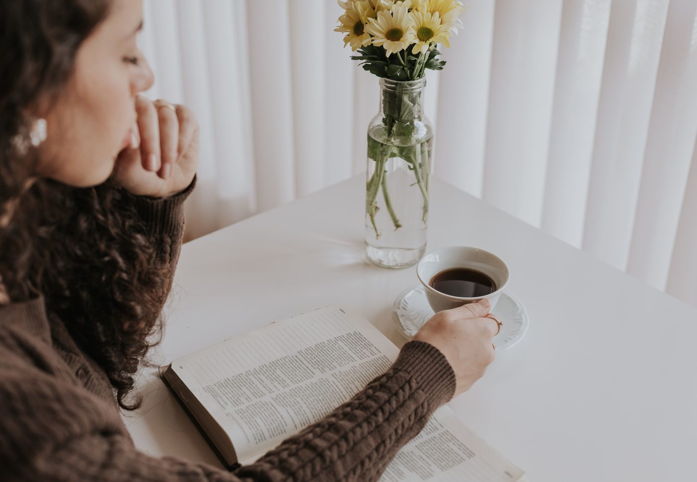 Mano con una taza de café junto a una Biblia abierta y margaritas amarillas